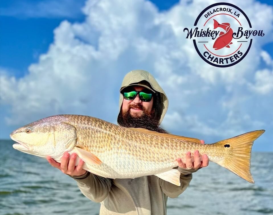 A man smiling as he fishes on a sunny day aboard a Whiskey Bayou Charter boat in the scenic waters of Delacroix, Louisiana.