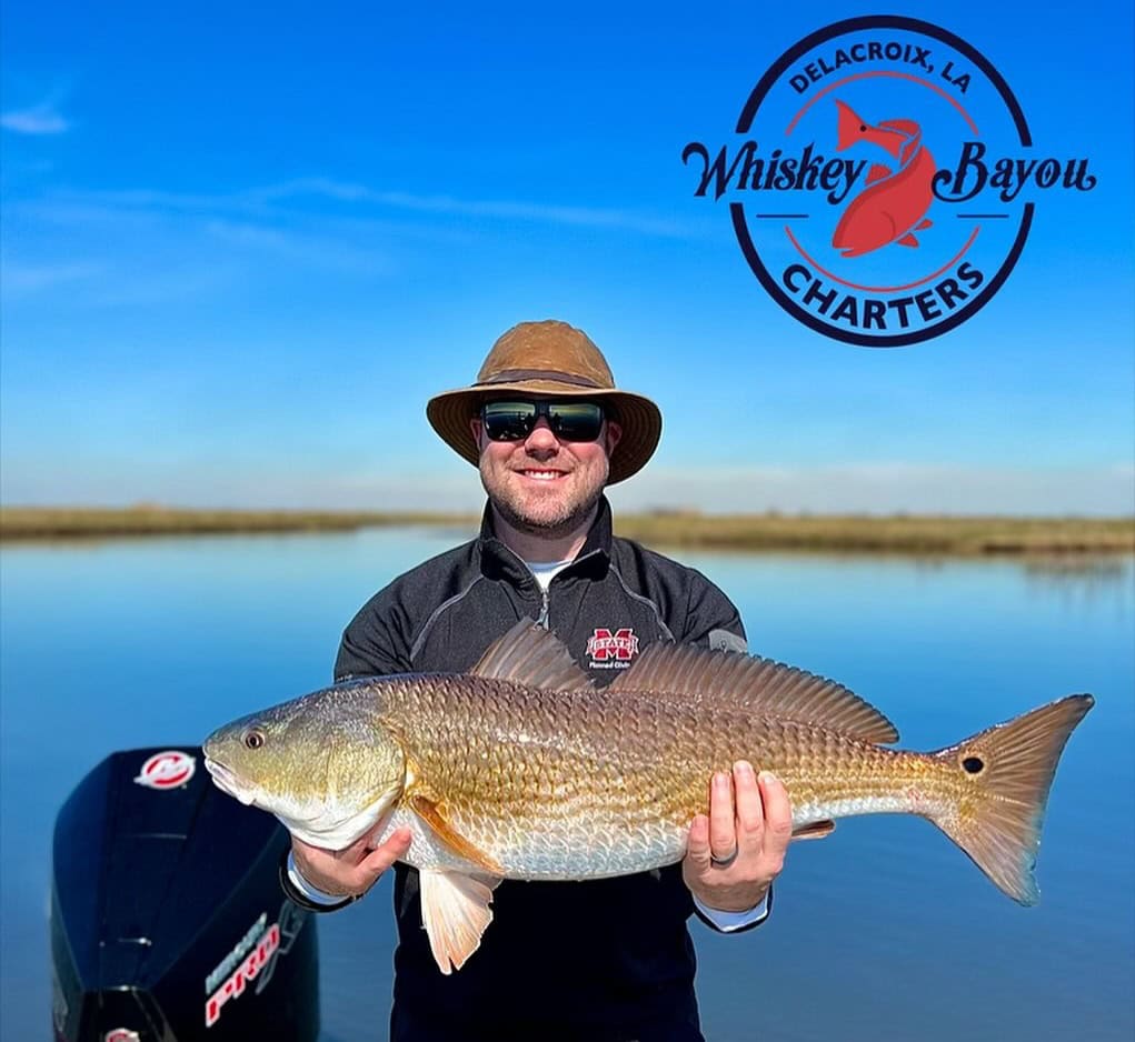 Man holding up a redfish from summer fishing in delacroix.