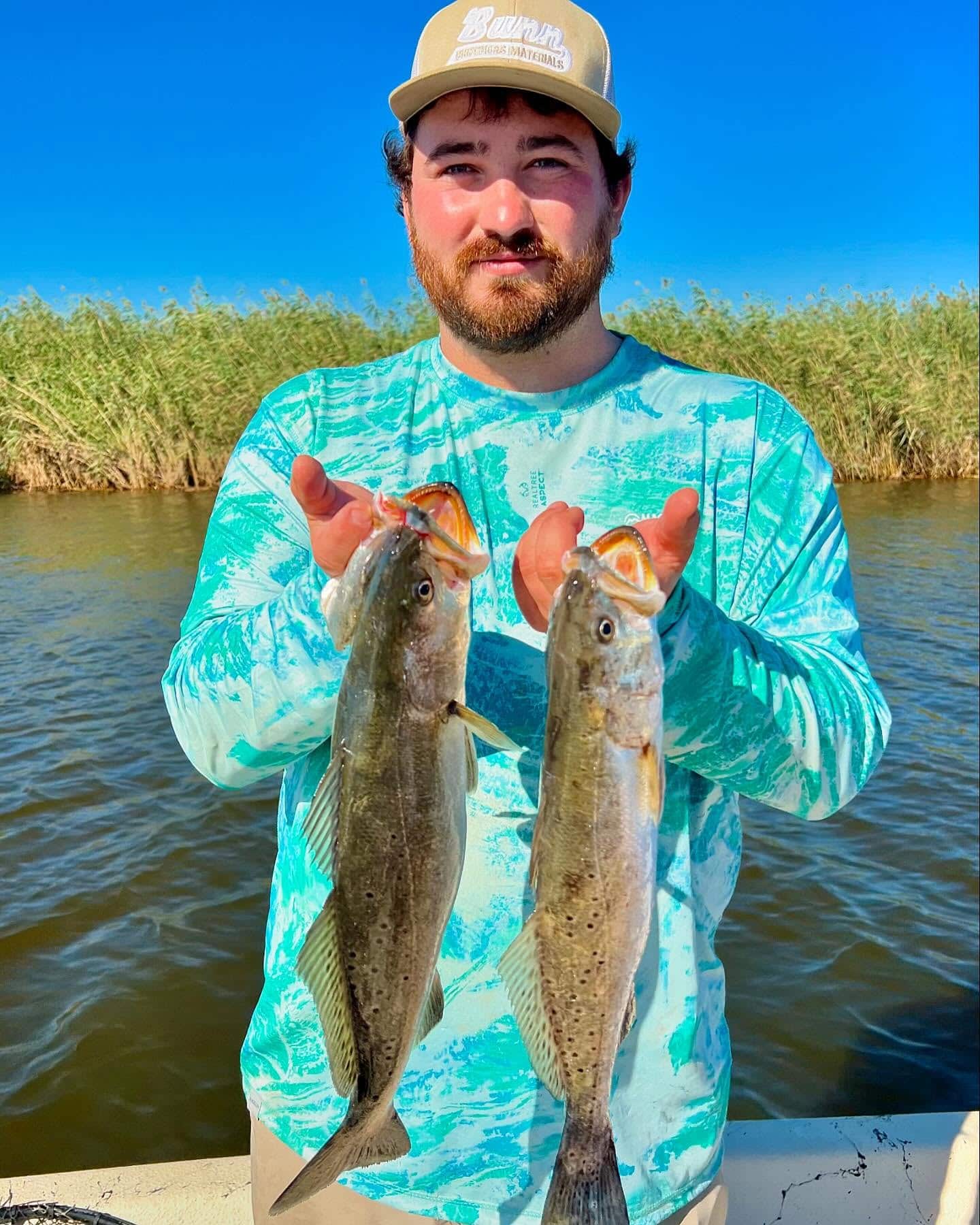 Man on a fishing charter holding up two speckled trout.