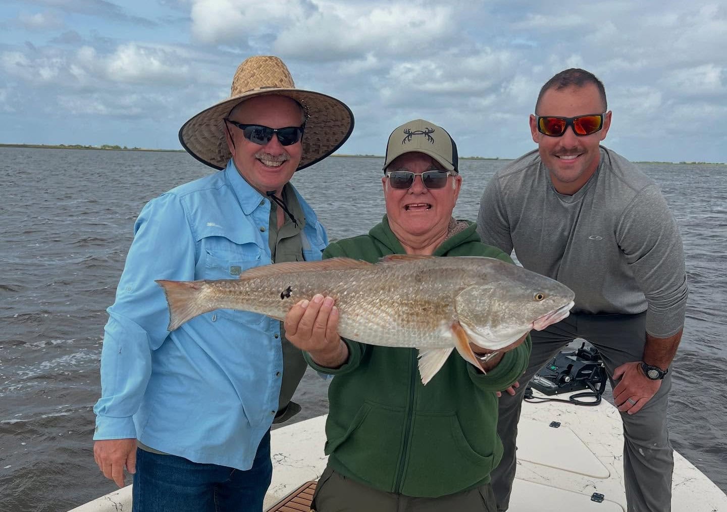 Three men holding a redfish caught while summer fishing in Louisiana.