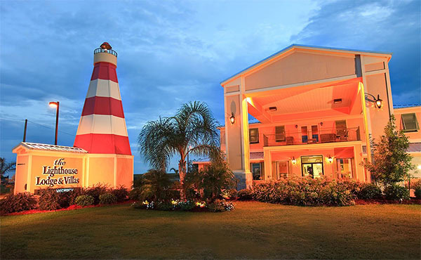 Frontal view of Lighthouse Inn hotel. Next to it is a red and white model of a lighthouse about the same size as the three story building.
