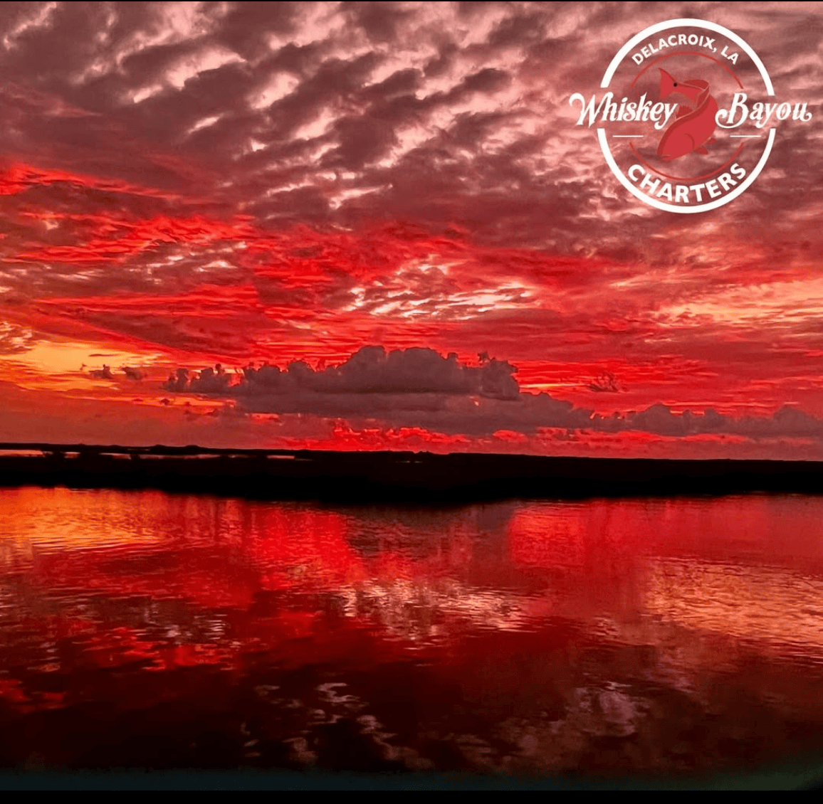 Ruby red skies during sunset. Clouds pattern the sky and the water of the marsh (broken up by dark silhouettes of land) reflect the colors above.