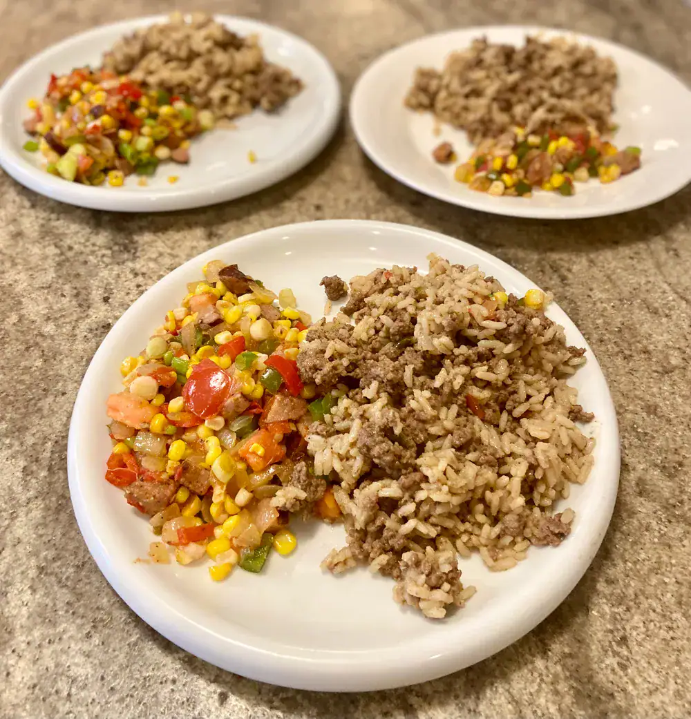 Dirty rice & Corn Maque Choux Combo Three white plates, each filled with dirty rice and Corn Maque Choux.