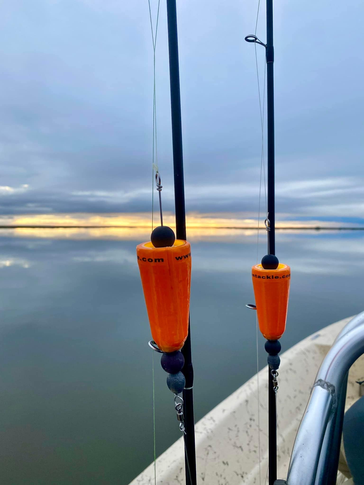 Two fishing poles set before a beautiful landscape shot of the Louisiana marsh. The water is calm and grey blue. The clouds in the sky mostly match the water, except for a small slice of yellow-orange cutting across the horizon.