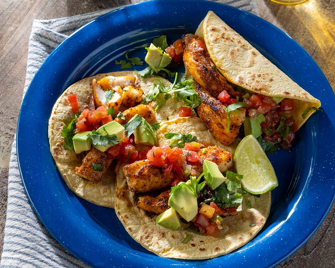 Blackened redfish tacos Three blackened fish tacos with lime and cilantro and diced tomato in a deep blue plate.