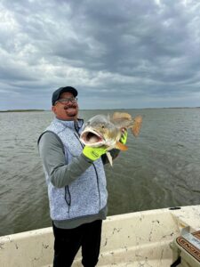 A man holding his catch up for the camera. He is holding the fish so it is facing the camera.