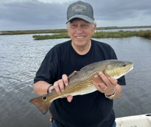 An older gentleman with a big smile, holding up his catch for the camera