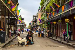 Image of iconic Bourbon Street in the French Quarter of New Orleans decorated in Mardi Gras Colors. Street performers occupy the middle of the street. 