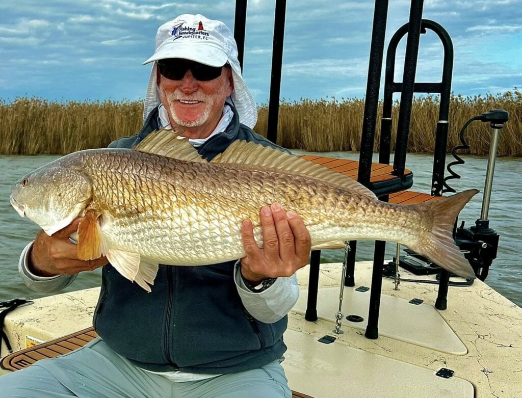 An angler sitting while holding up his catch for the camera.