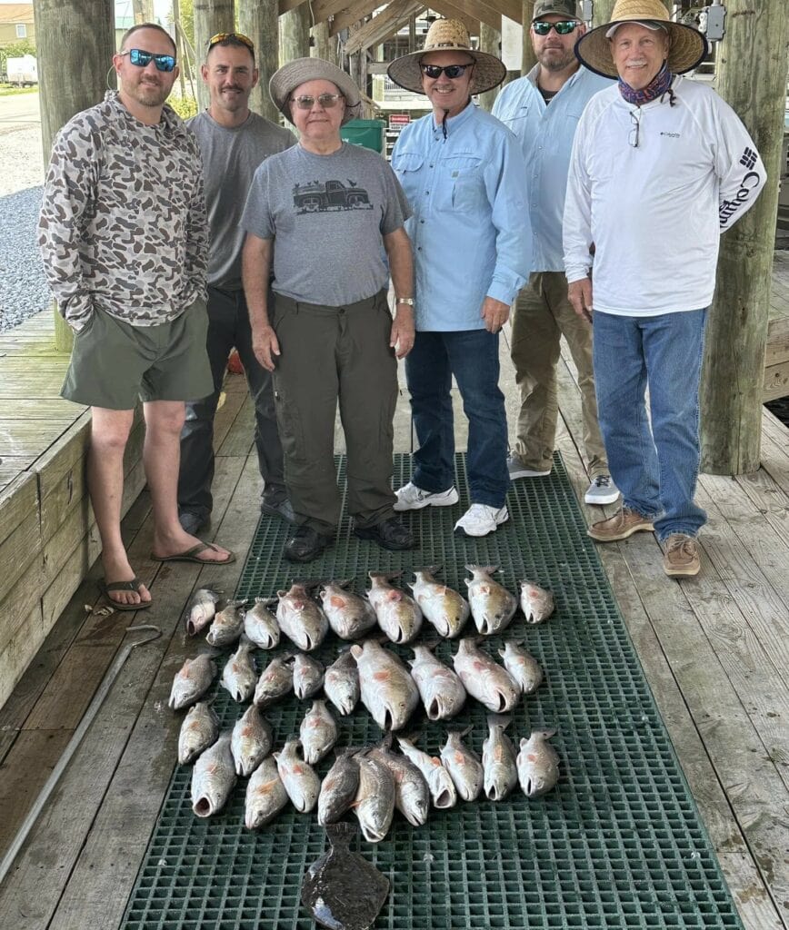 Six men standing proudly together in front of their catch, consisting of three dozen fish. 