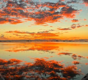 A beautiful sunrise painting the clouds and sky above and water below in rich pinks, oranges, and yellows.