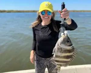 A woman holding up a zebra striped sheepshead fish for the camera